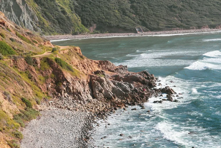 Woman and border collie hiking a coastal trail along the Pacific Coast Highway in California